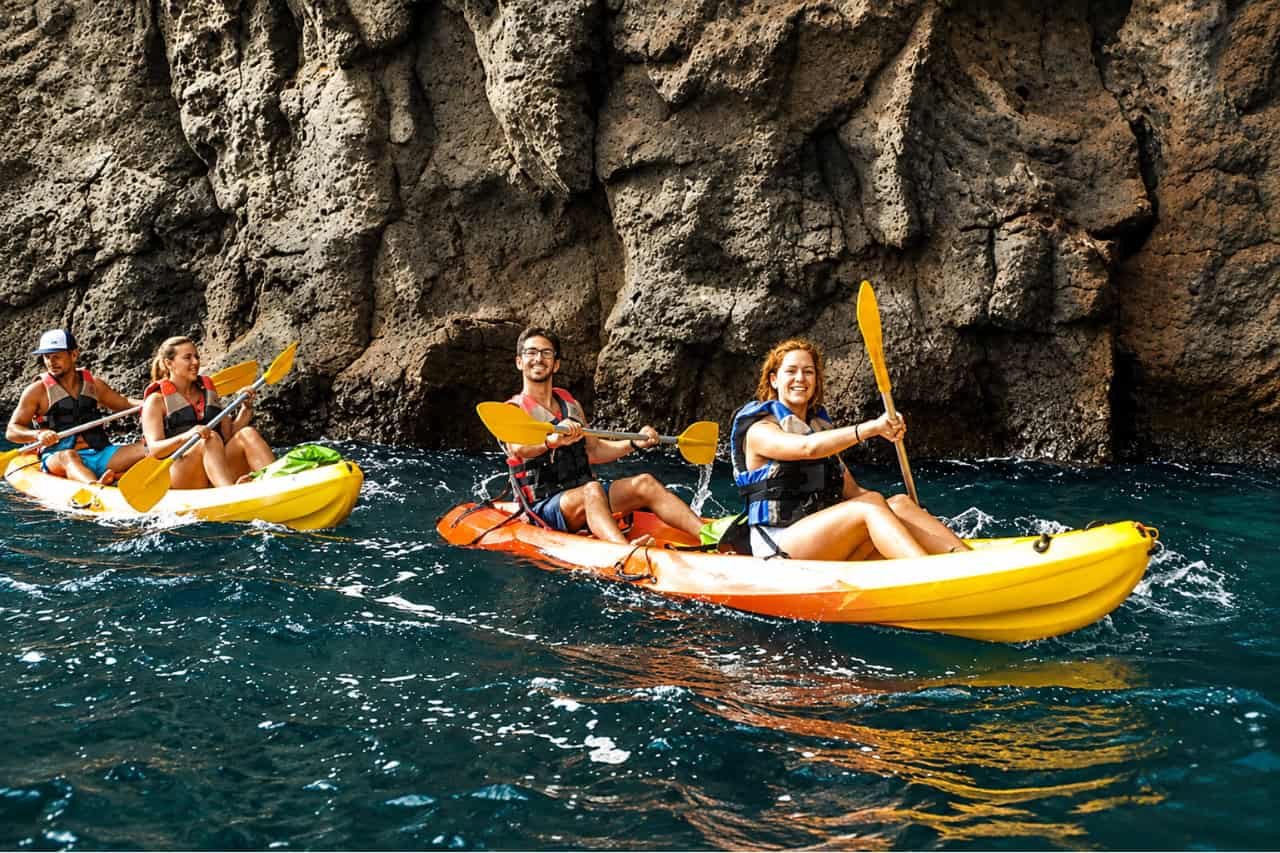 Group kayaking beside rugged volcanic cliffs during a guided sea kayaking tour in Gran Canaria.