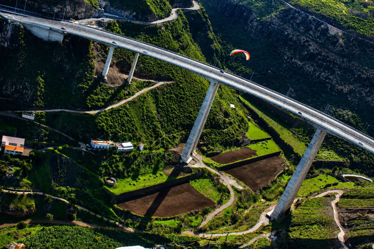 Gleitschirmflieger über einem dramatischen Bergtal und einer hohen Brücke während eines Gleitschirmflieger-Erlebnisses auf Gran Canaria.