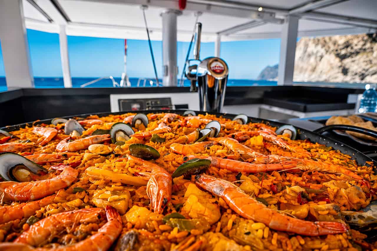 Paella de marisco fresco servida a bordo durante un alquiler privado de catamarán en Gran Canaria, con langostinos, mejillones y arroz con azafrán preparado para los invitados en el mar.