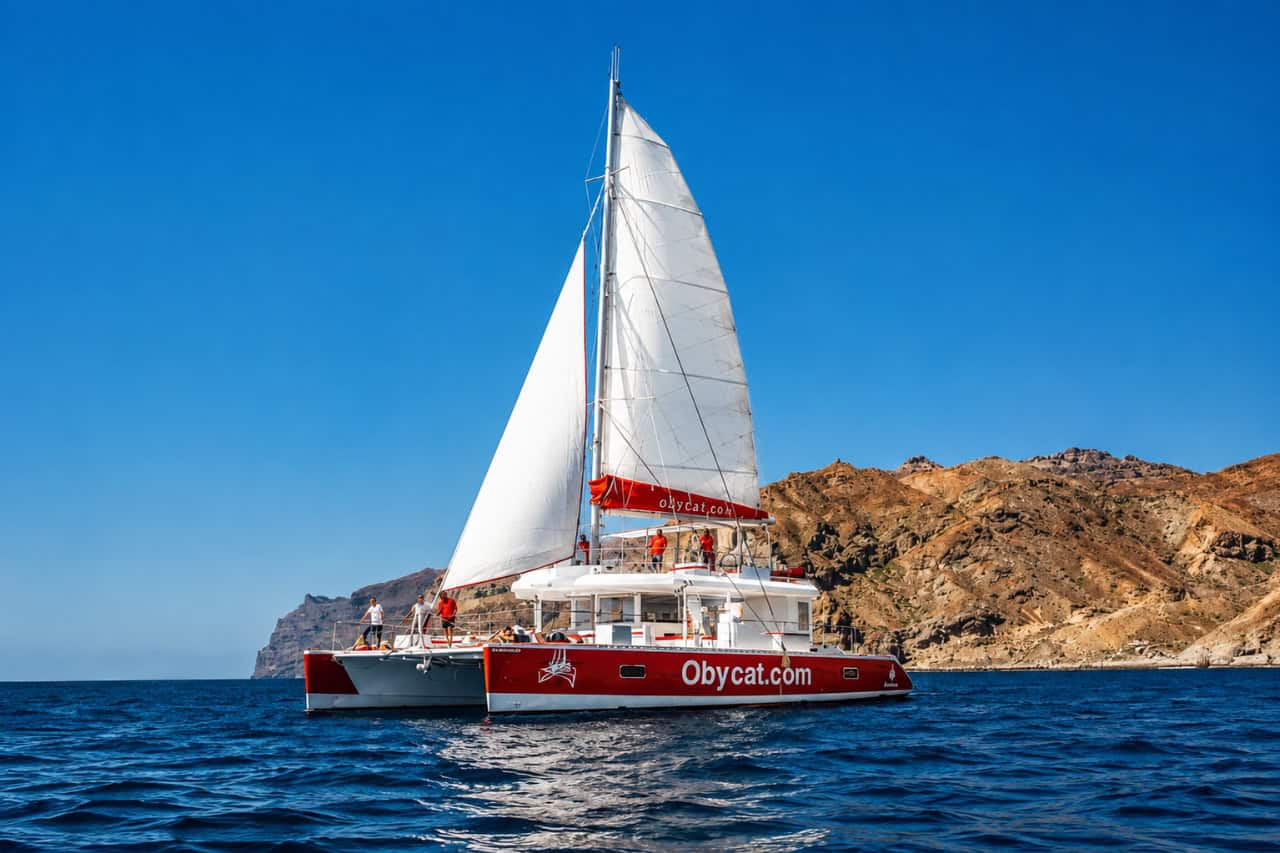 Lujoso catamarán privado navegando por la costa de Gran Canaria durante un alquiler de catamarán privado con mar azul cristalino y acantilados escarpados de fondo.