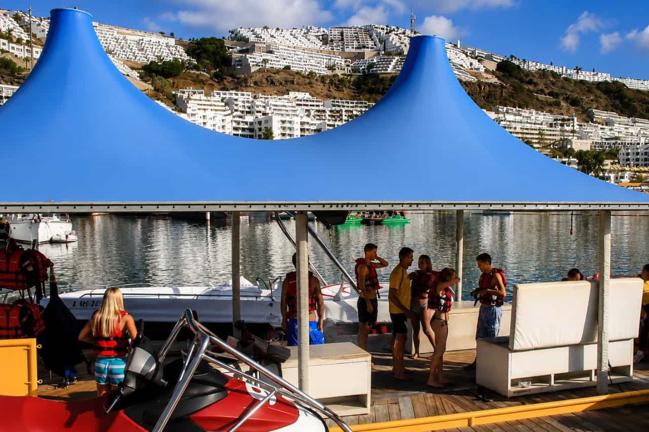 Huéspedes preparándose para una actividad de moto acuática en un centro de deportes náuticos en Gran Canaria, con chalecos salvavidas, motos de agua y vistas al puerto deportivo.
