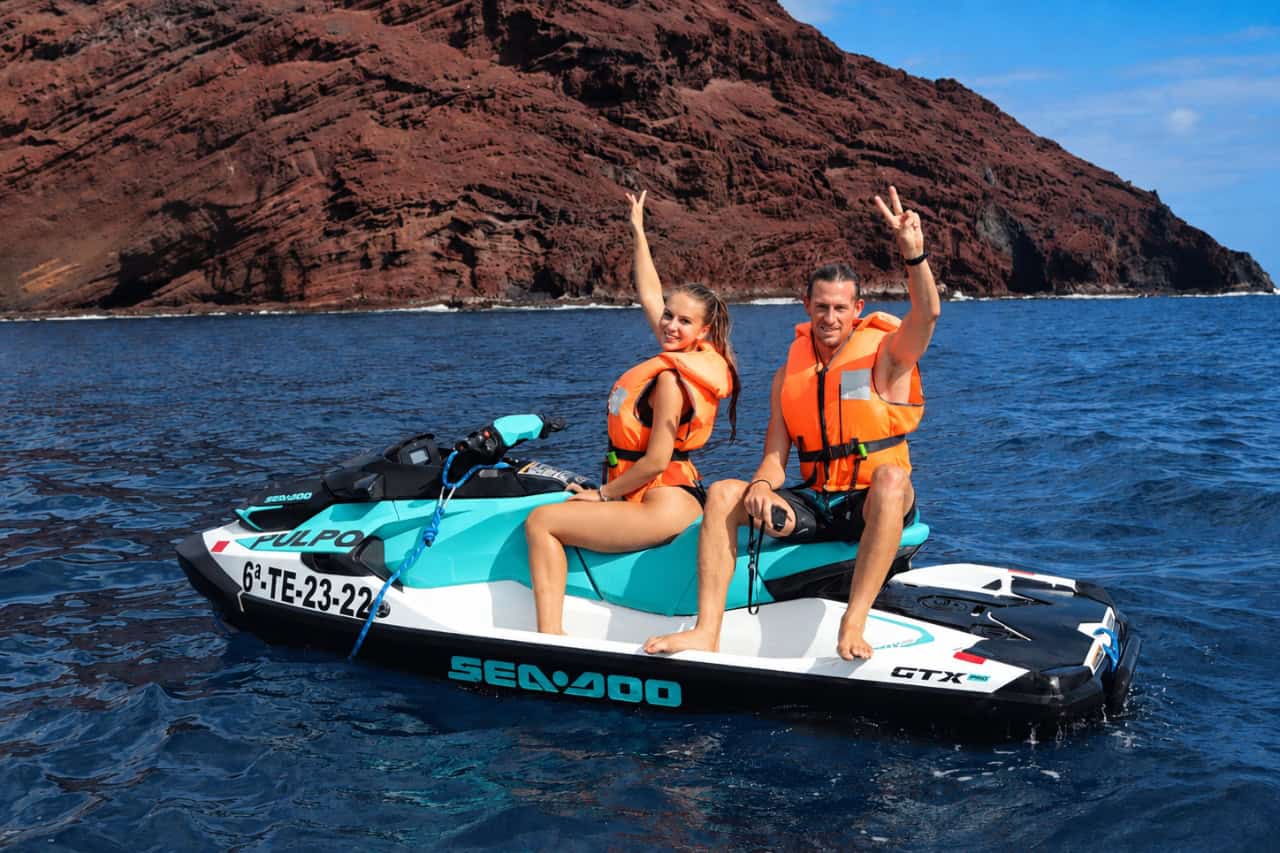 Couple posing on a jet ski beside Tenerife’s dramatic volcanic coastline during a guided ocean jet ski tour.
