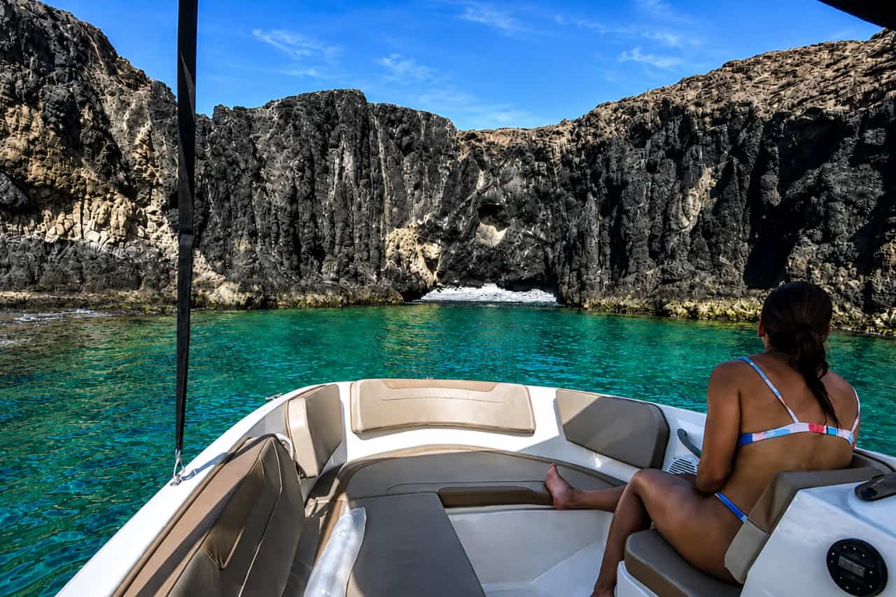 Passenger relaxing on a self-drive boat rental without a licence in Lanzarote, surrounded by turquoise water and volcanic cliffs.