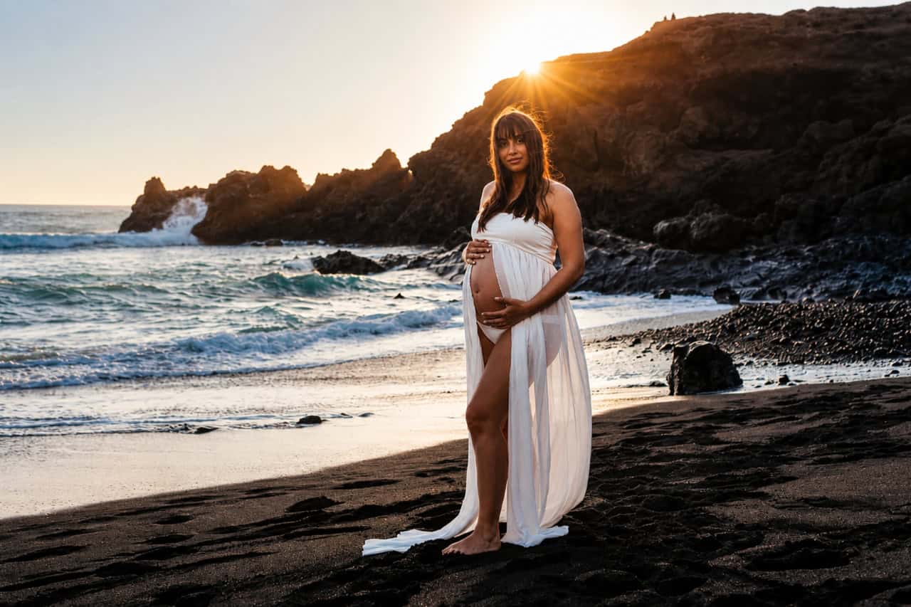 Schwangere Frau bei einem Strand-Fotoshooting auf Lanzarote bei Sonnenuntergang an einem Vulkanstrand, aufgenommen von einem professionellen Fotografen auf Lanzarote.