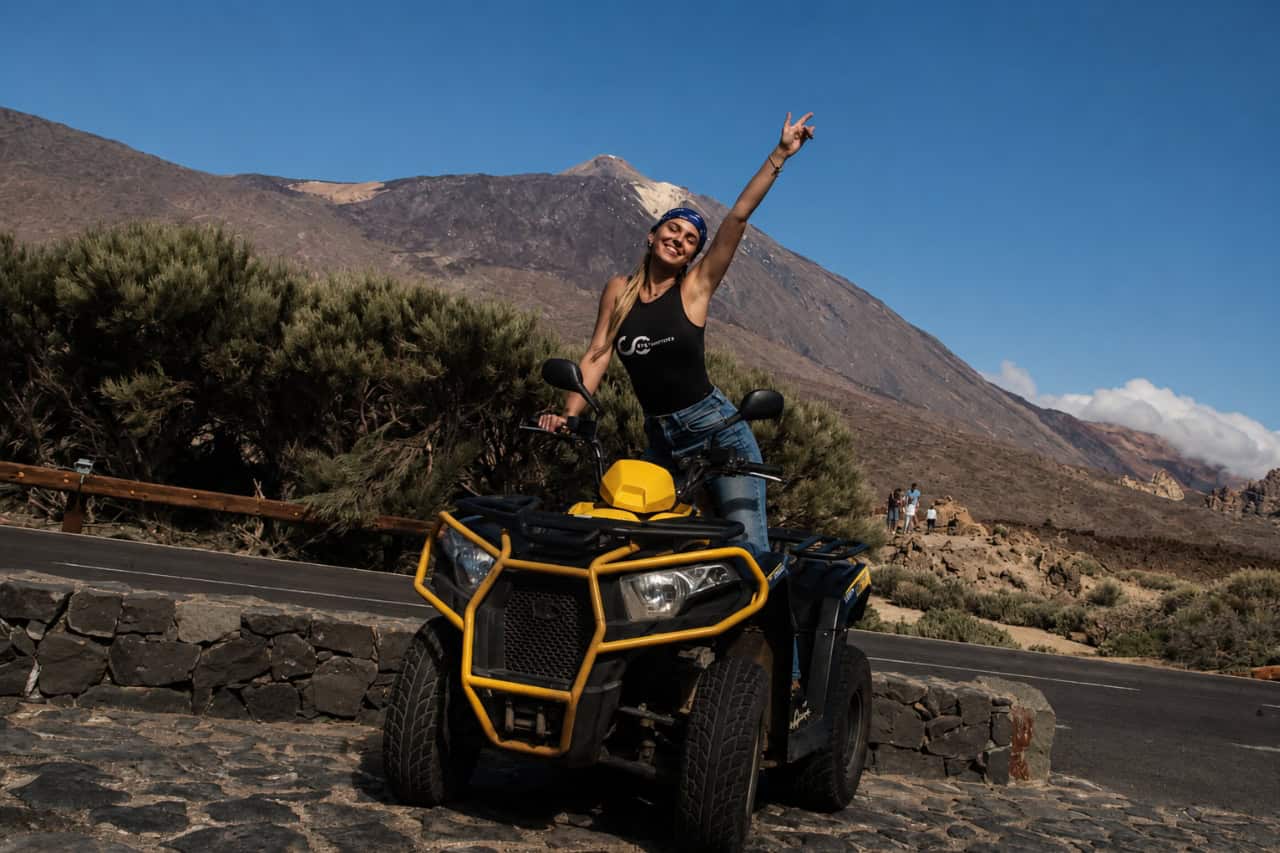 Smiling woman posing on a black and yellow quad with Mount Teide and Tenerife’s volcanic landscape behind her.