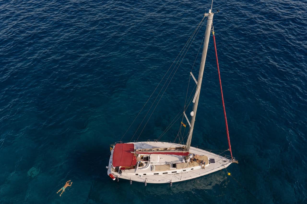 Aerial view of the Atlantic Star private sailing boat anchored in clear water near Puerto Colón, with a guest swimming beside the yacht.