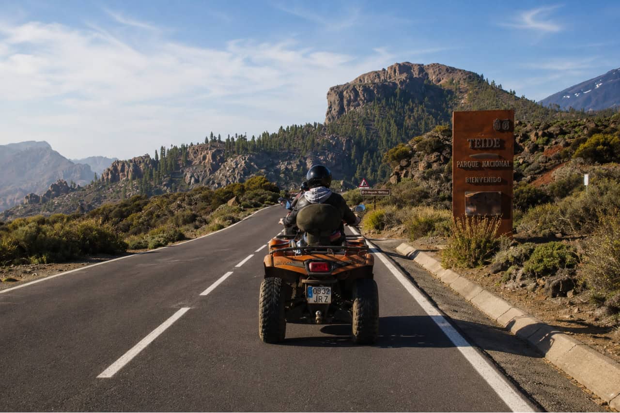 : Rider travelling by quad along a mountain road beside the Teide National Park entrance sign during a scenic Tenerife quad safari.
