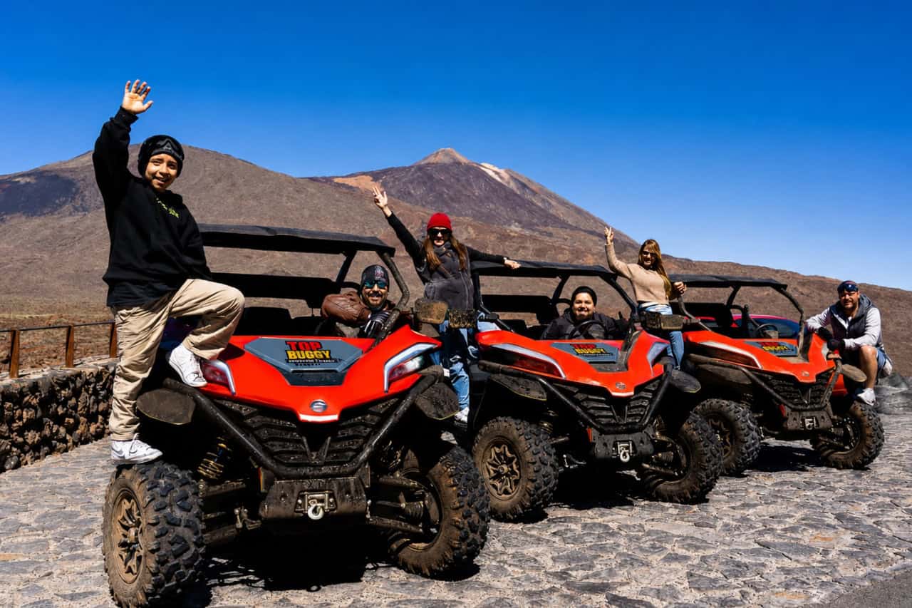 Group of travellers posing with red buggies in front of Mount Teide during a guided Tenerife buggy adventure.