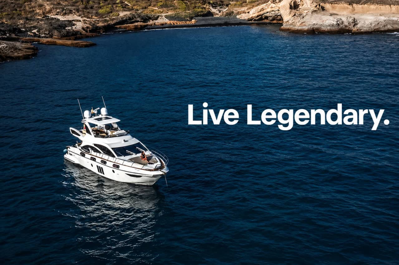 Aerial view of a white luxury yacht anchored beside Tenerife’s volcanic coastline with the words “Live Legendary” across the ocean.