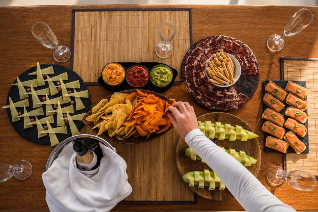 Overhead view of premium yacht catering with cured meats, cheese, salmon, fruit, dips, tortilla chips and chilled champagne.