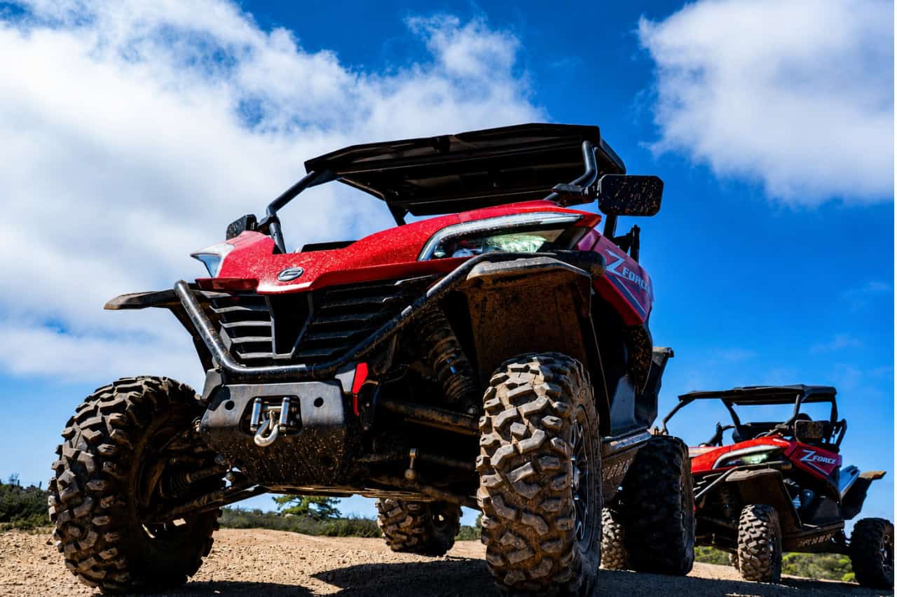 Low-angle close-up of two red off-road buggies with large tyres on a rugged Tenerife trail beneath a bright blue sky.