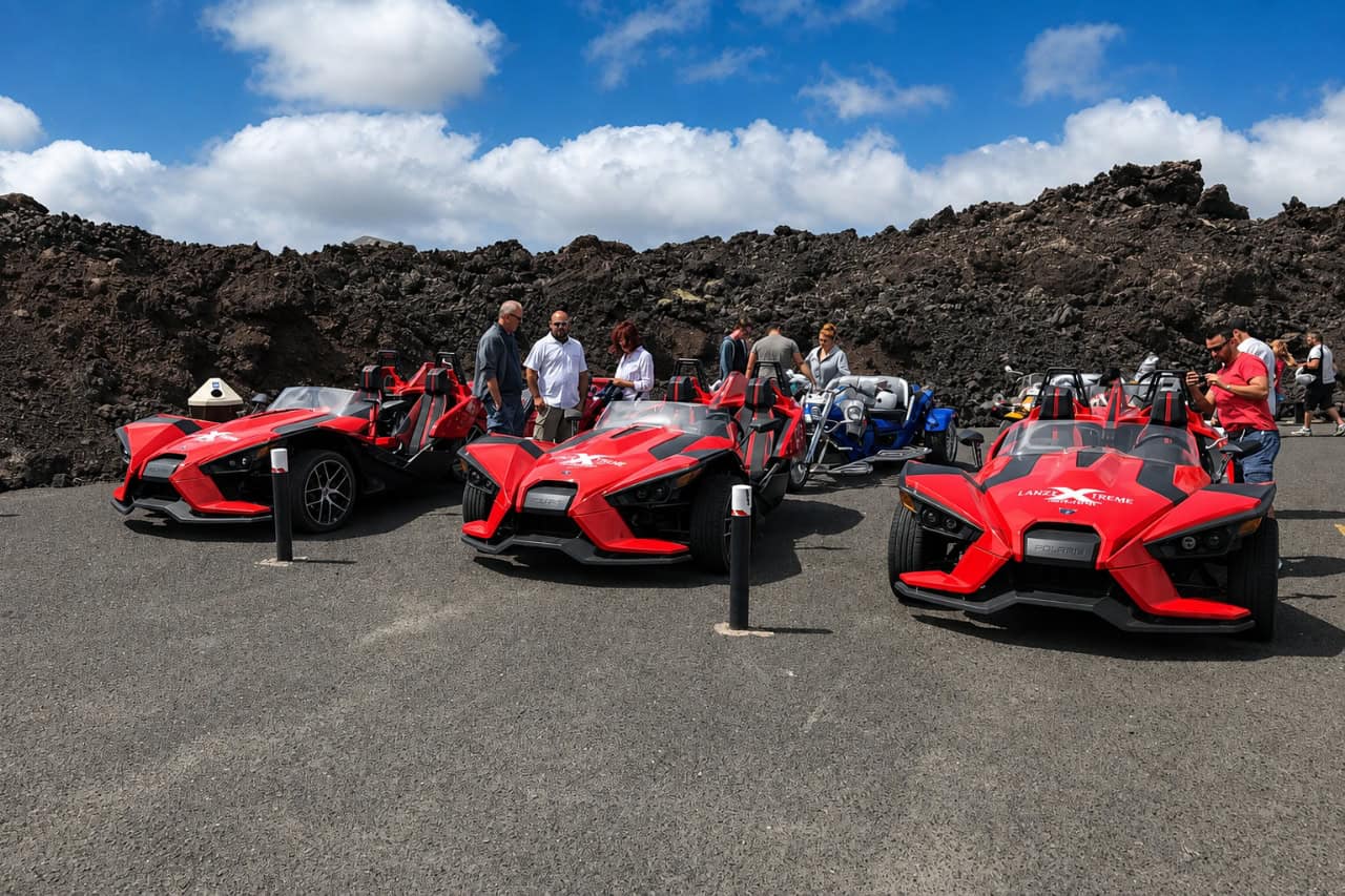 Polaris Slingshot Lanzarote Tour Three red Polaris Slingshot cars on a volcanic road during a guided Lanzarote Slingshot tour.