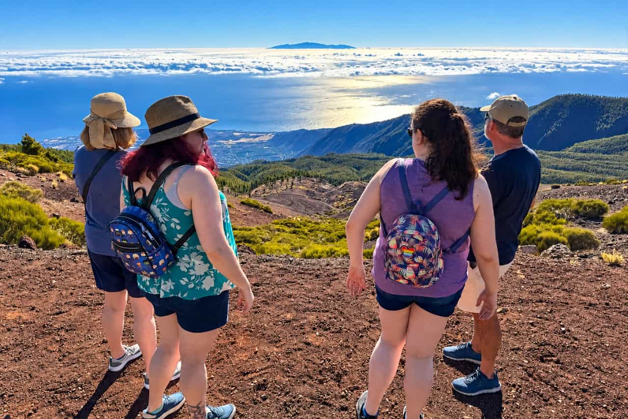 Four travellers on a high volcanic viewpoint in Tenerife looking over a sea of clouds