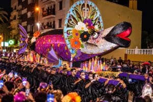The giant decorated sardine of the Entierro de la Sardina carried through Santa Cruz de Tenerife at night by mourners in black robes with painted skull faces, surrounded by candles and crowds