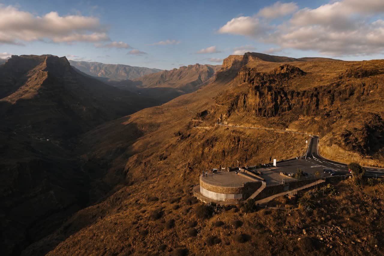 Panoramablick auf die schroffen Vulkantäler und Serpentinenstraßen Gran Canarias im warmen Abendlicht.