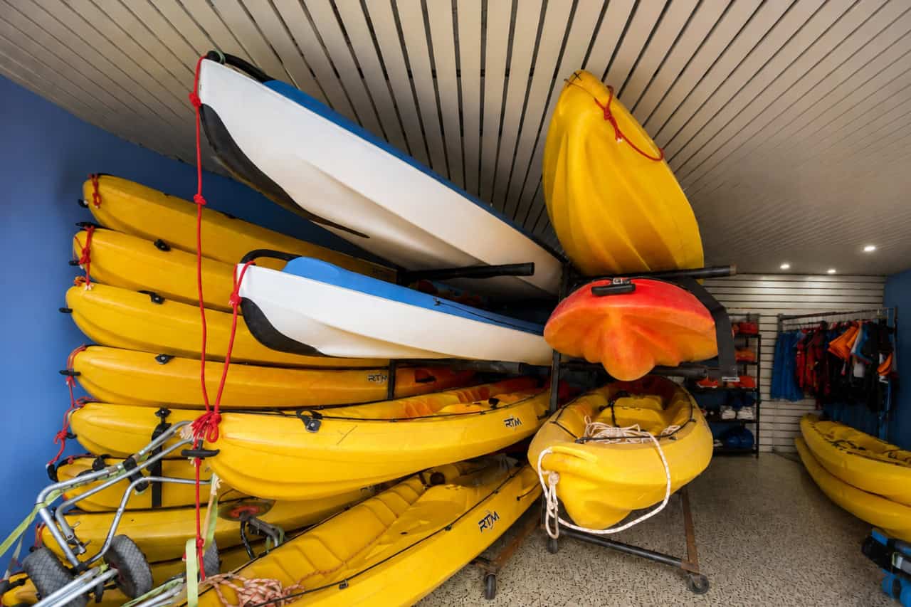 Large selection of yellow, white and orange kayaks stored with paddles and life jackets at a Tenerife kayaking centre, showing the equipment prepared for guided kayak and snorkeling excursions.
