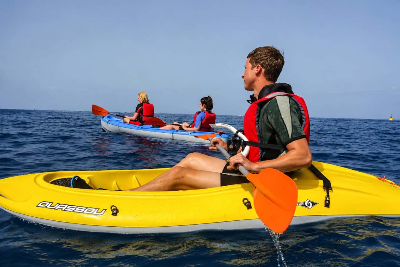 Guests paddling colourful kayaks across the Atlantic Ocean during a guided kayaking experience in Tenerife, wearing life jackets and using double-ended paddles while exploring the coast together.