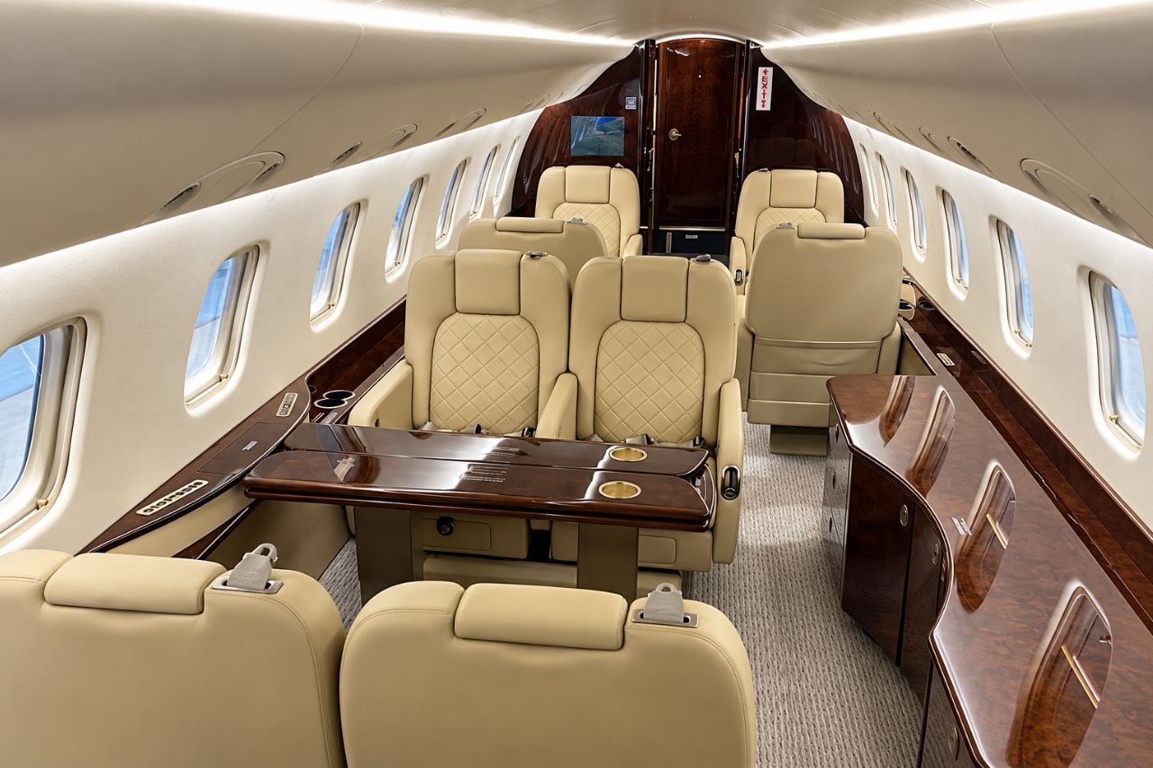 Private jet cabin with cream leather club seats facing each other and wooden tables