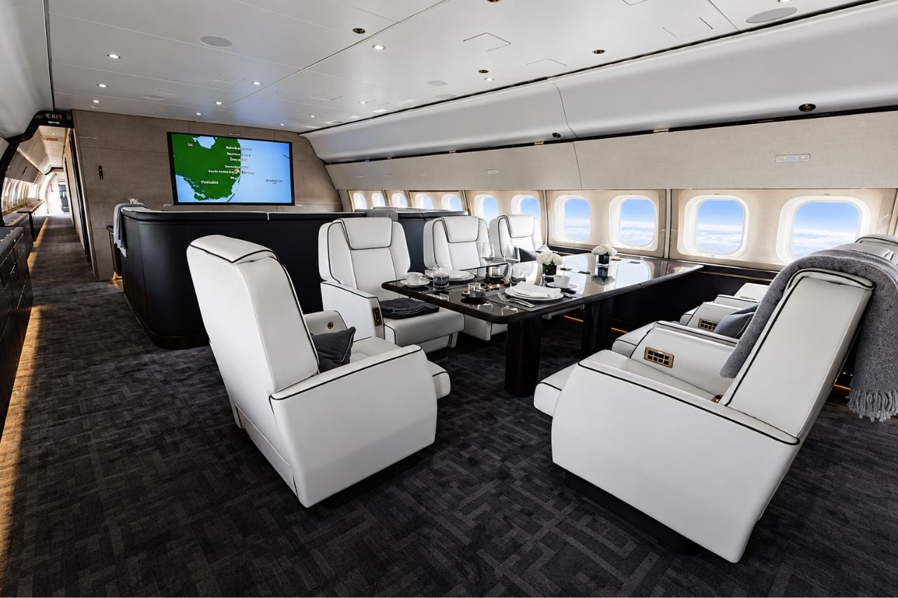 VIP airliner lounge interior with white leather armchairs, dining table and widescreen