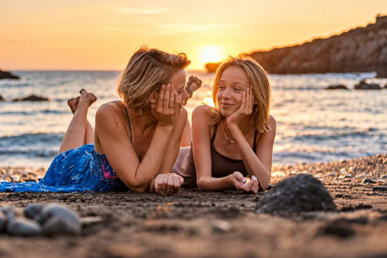 Moeder en dochter liggen op het strand en lachen terwijl ze een zonsondergang fotograferen op Tenerife
