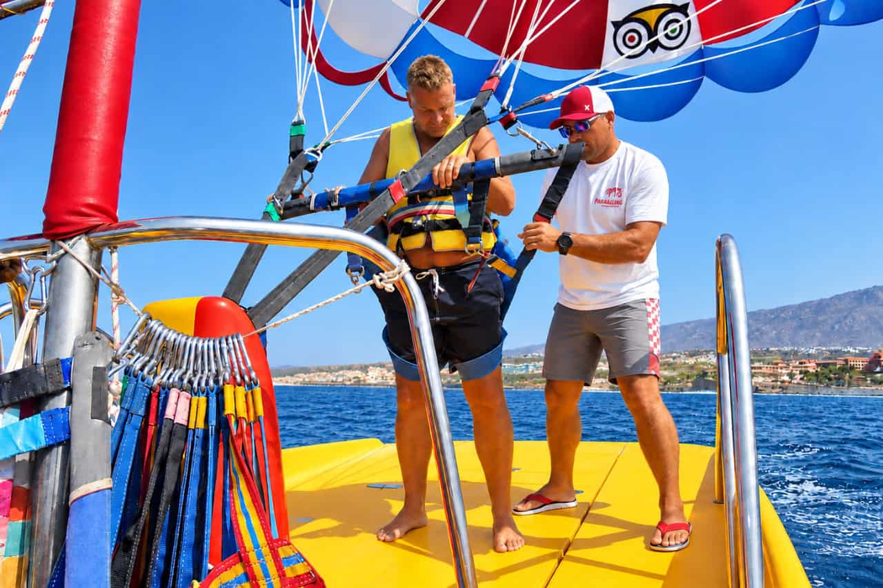Crew fitting a parasailing harness to a guest on the yellow boat off the Tenerife coast