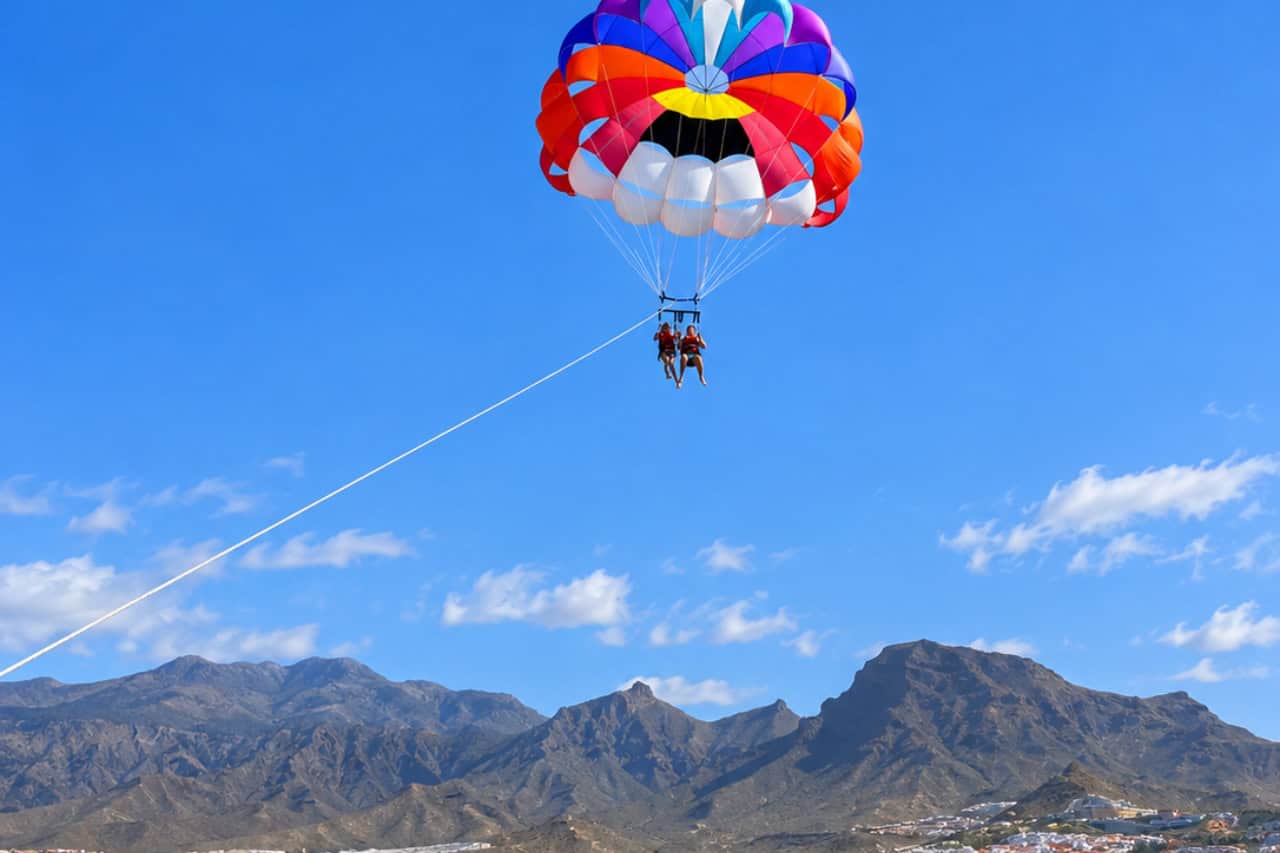 Two guests parasailing high above the ocean with the mountains of Costa Adeje behind