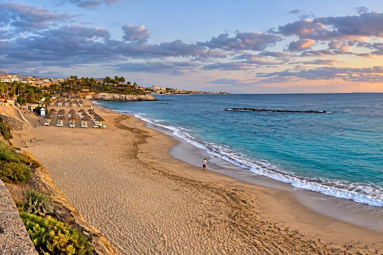 Playa del Duque strand in Costa Adeje met ligbedden, goudkleurig zand en turquoise water, de gebruikelijke fotostop