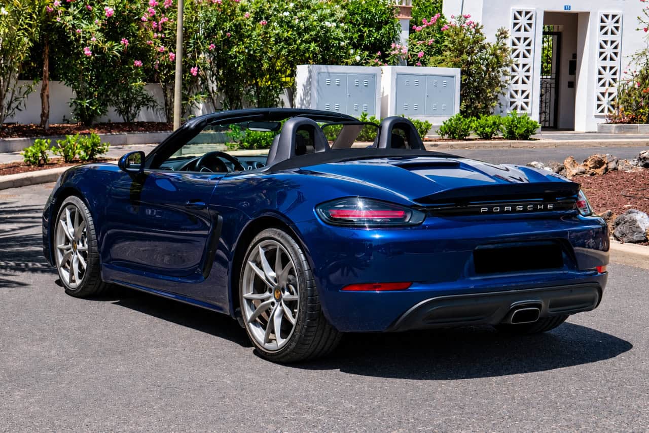 Rear view of a blue Porsche 718 Boxster convertible with the roof down, available for luxury car rental in Tenerife.