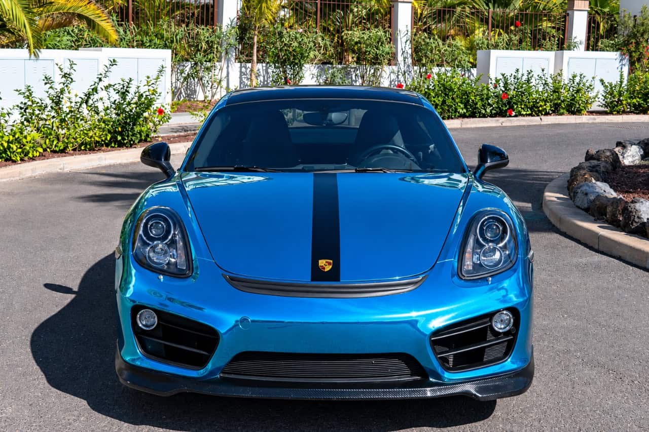 Front view of a teal blue Porsche 718 Cayman sports coupe with a black racing stripe, available for luxury car rental in Tenerife.