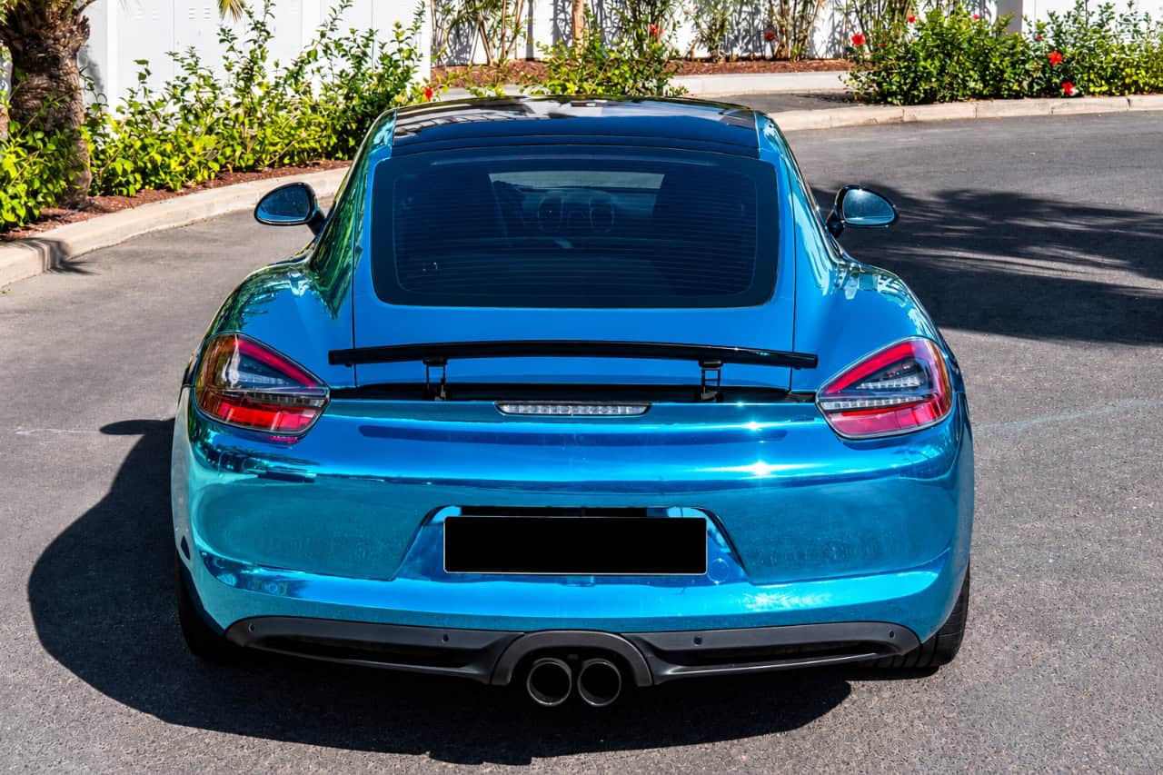 Rear view of a blue Porsche 718 Cayman with a rear spoiler and central dual exhaust, available for sports car rental in Tenerife.