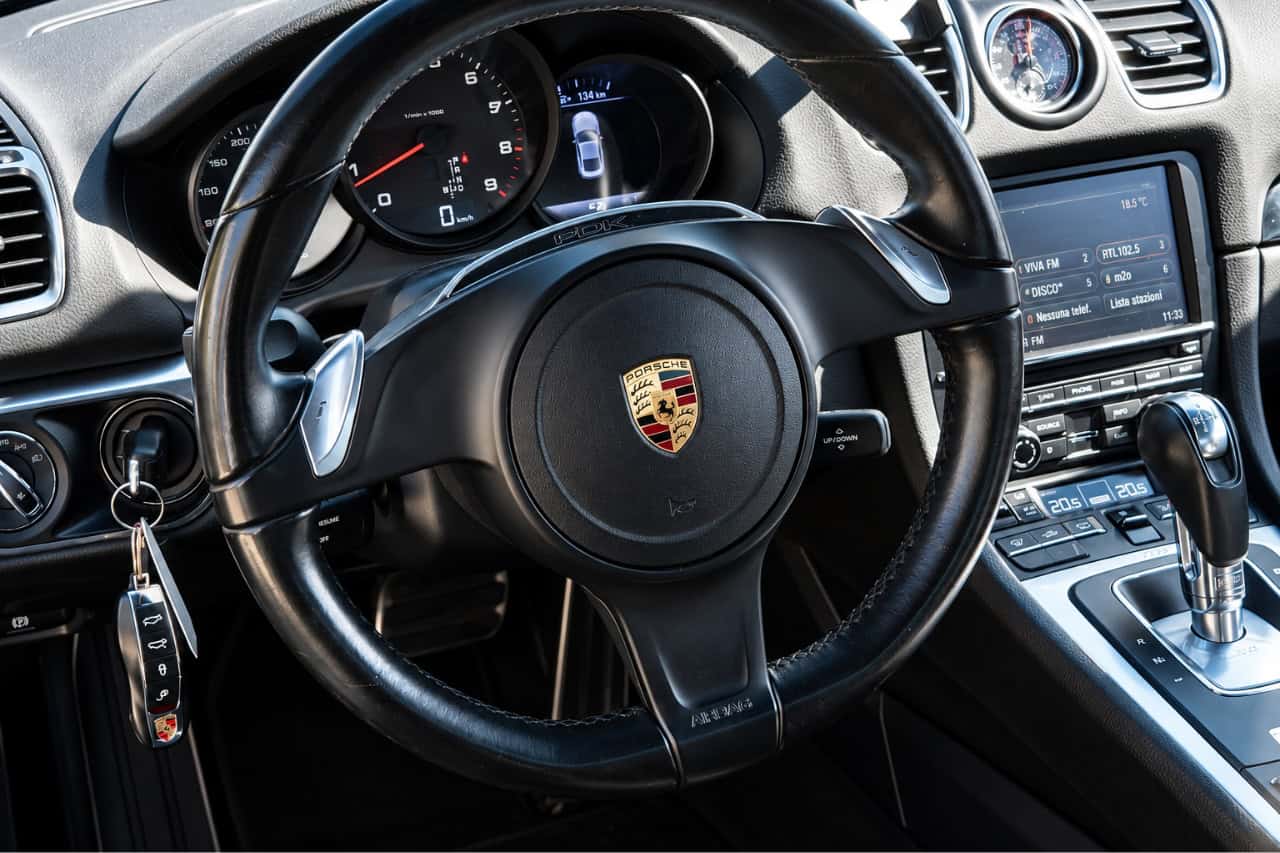 Driver’s view inside a Porsche Cayman featuring the leather steering wheel, paddle shifters, dashboard and automatic transmission.