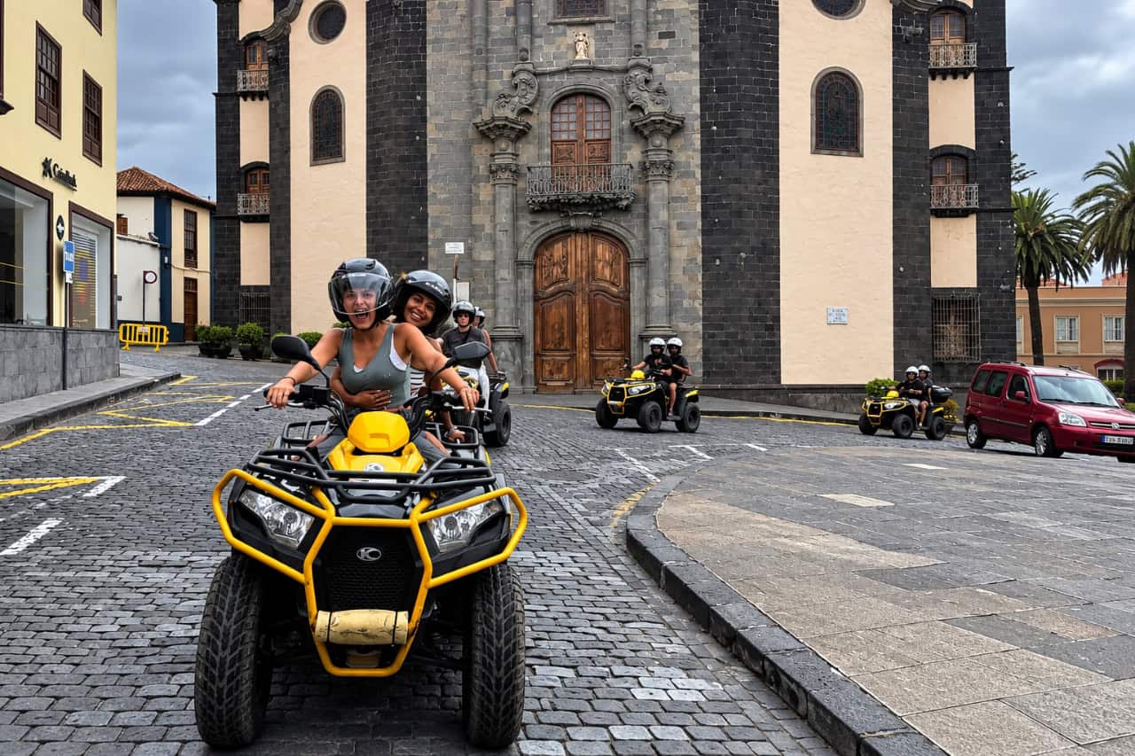 Firhjulede knallerter kører over en brostensbelagt plads foran en gammel kirke i det nordlige Tenerife