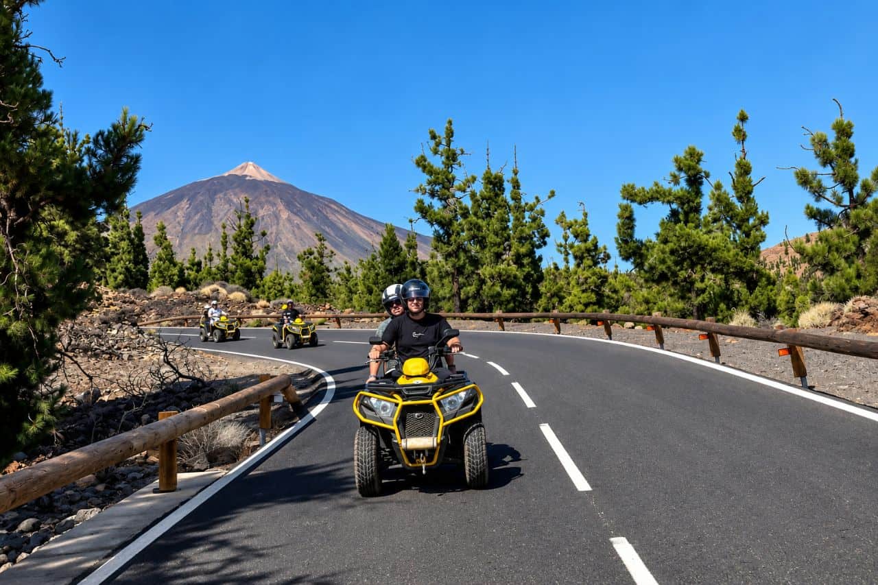Guests riding yellow quad bikes along a scenic mountain road with Mount Teide and Tenerife pine forest in the background.