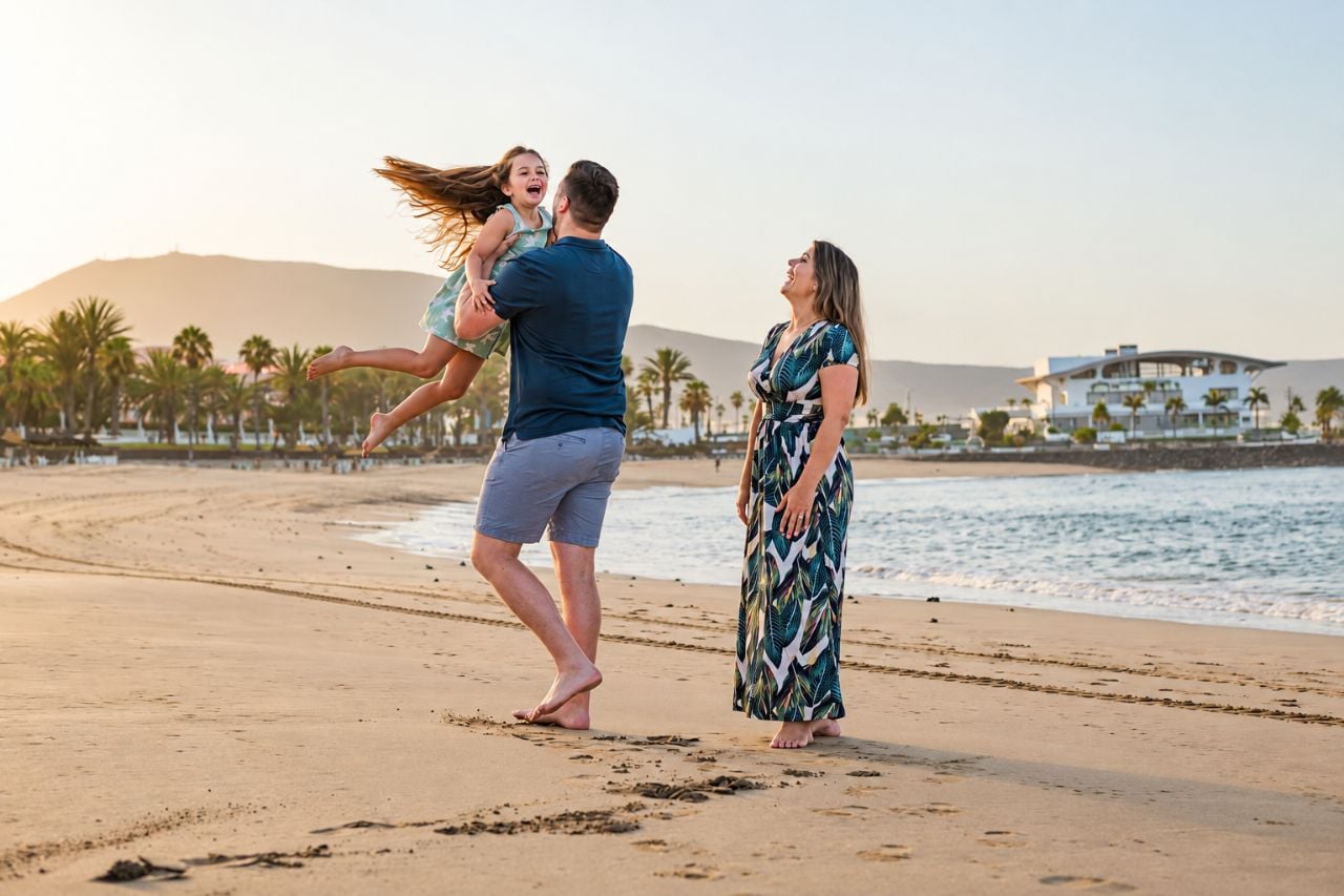 Vader houdt zijn dochter in de lucht terwijl de moeder lacht tijdens een fotoshoot op het strand van Tenerife