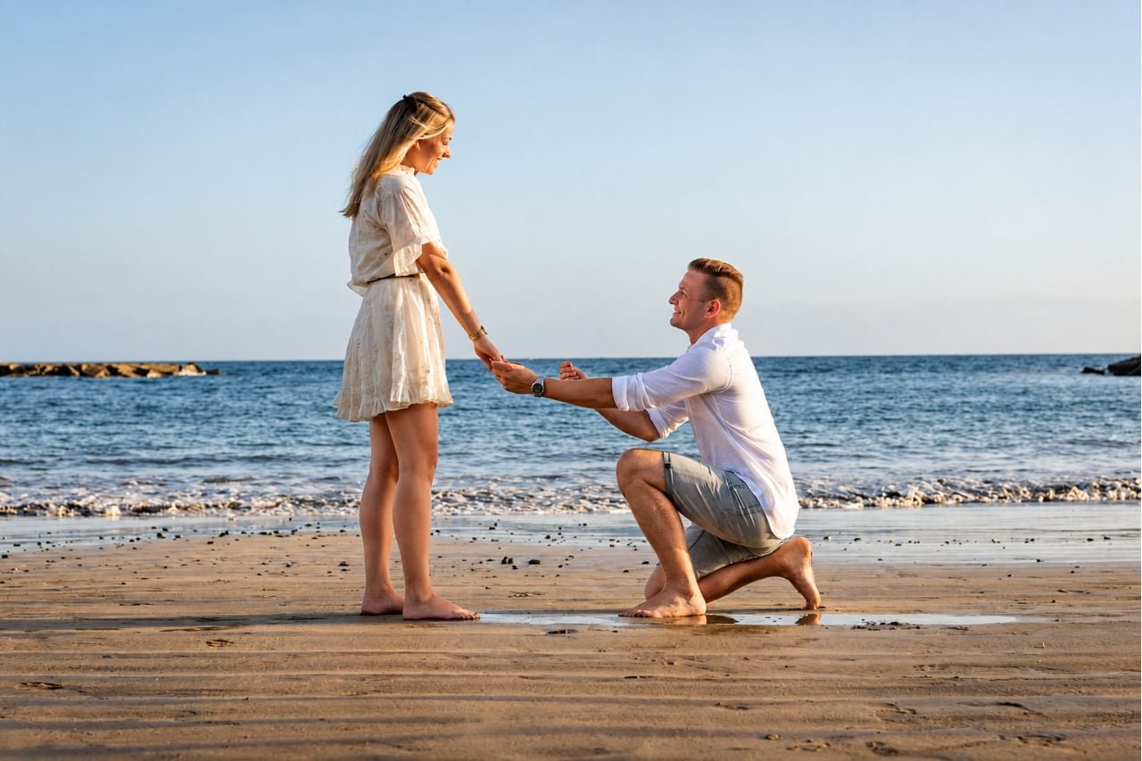 Man op een knie dat een Playa del Duque aanzoek doet bij de Atlantische Oceaan in het warme avondlicht