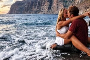 Couple sharing a romantic moment by the ocean during a professional photoshoot in Tenerife, with dramatic coastal cliffs in the background.