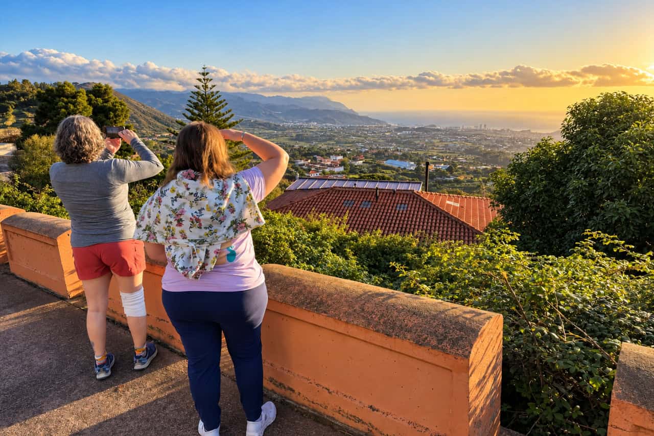 Two travellers photographing a green valley and the coast from a hillside viewpoint in Tenerife