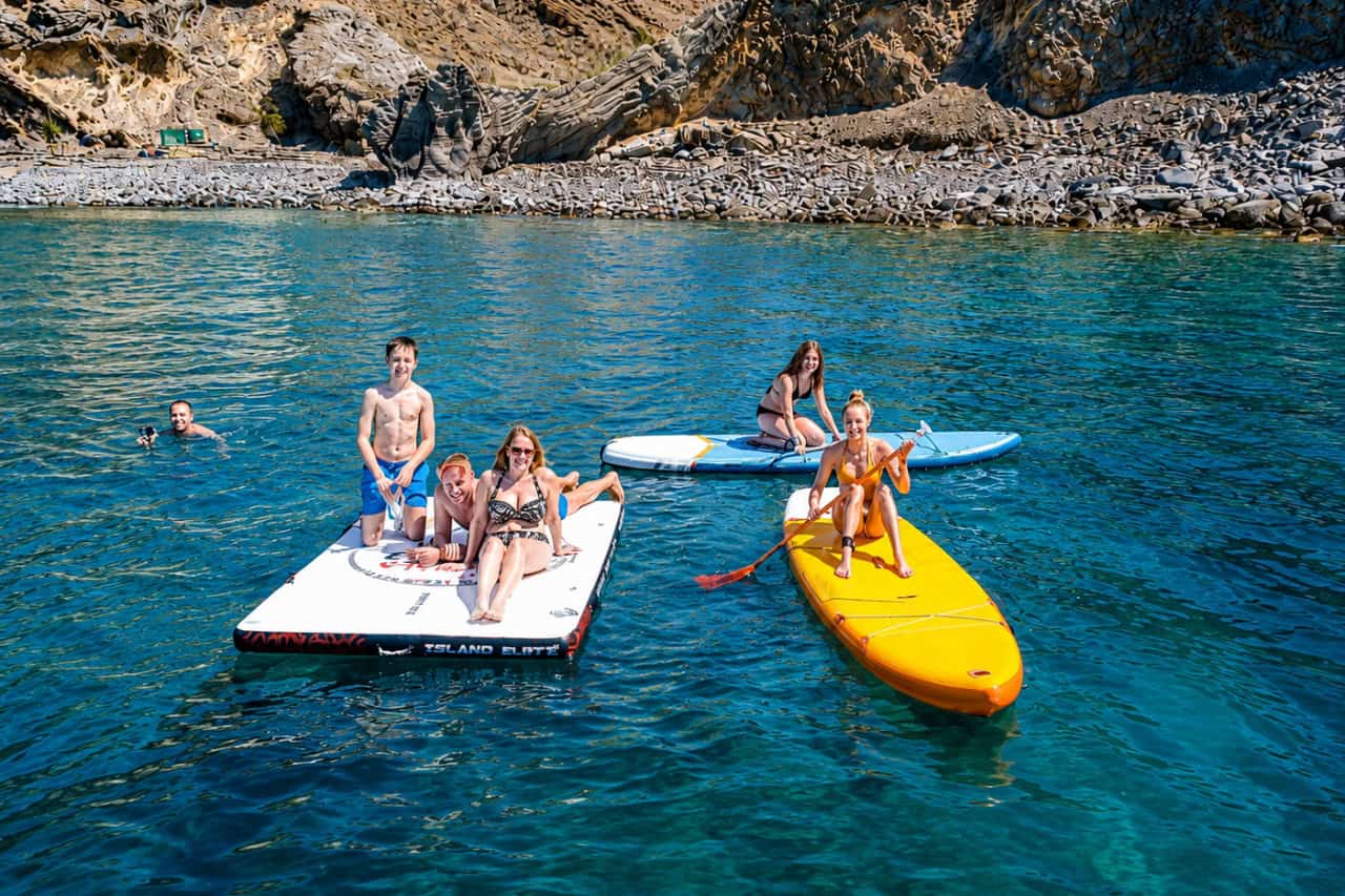 Guests paddleboarding and swimming beside the rocky coast of Gran Canaria during the Blue M swim stop