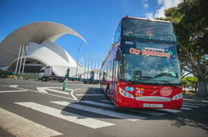 Red City Sightseeing double-decker bus beside the white curved Auditorio de Tenerife in Santa Cruz.